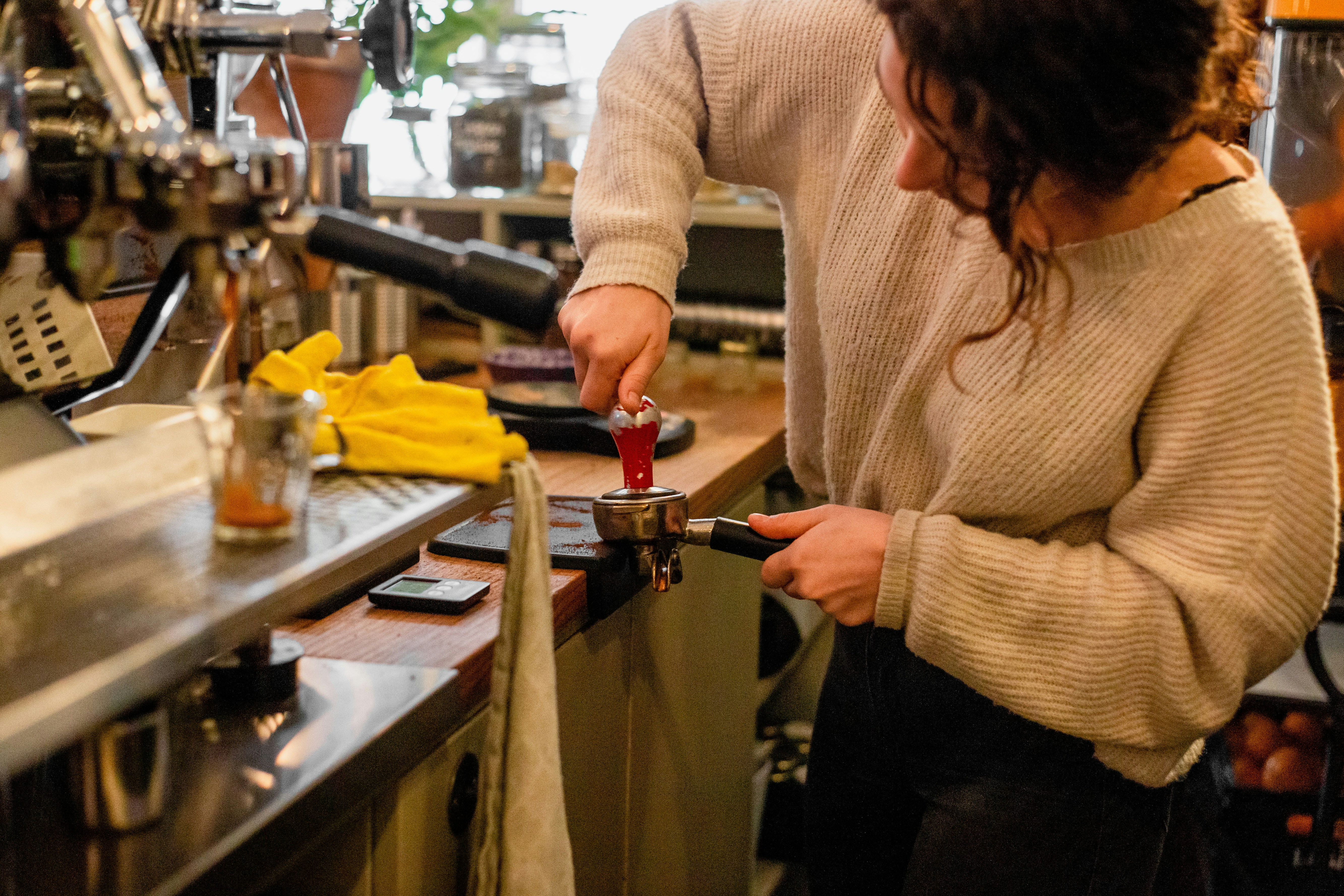 Woman in a beige sweater making coffee at an espresso machine