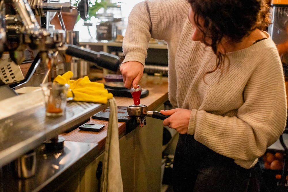 woman in beige sweater holding silver and red faucet