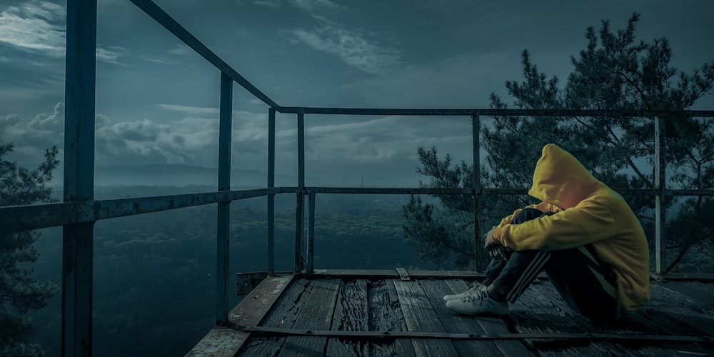 man in yellow jacket sitting on wooden dock during daytime