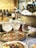 A luxurious dining setting featuring a bucket filled with several bottles of wine on ice, accompanied by a tray with elegant glasses containing icy drinks. In the foreground, there is a plate with a finely arranged meal, including grilled bread topped with a garnish, resembling herbs or vegetables, and a dollop of what appears to be cheese. The background shows a variety of blurred bottles, adding to the ambiance of a refined setting.