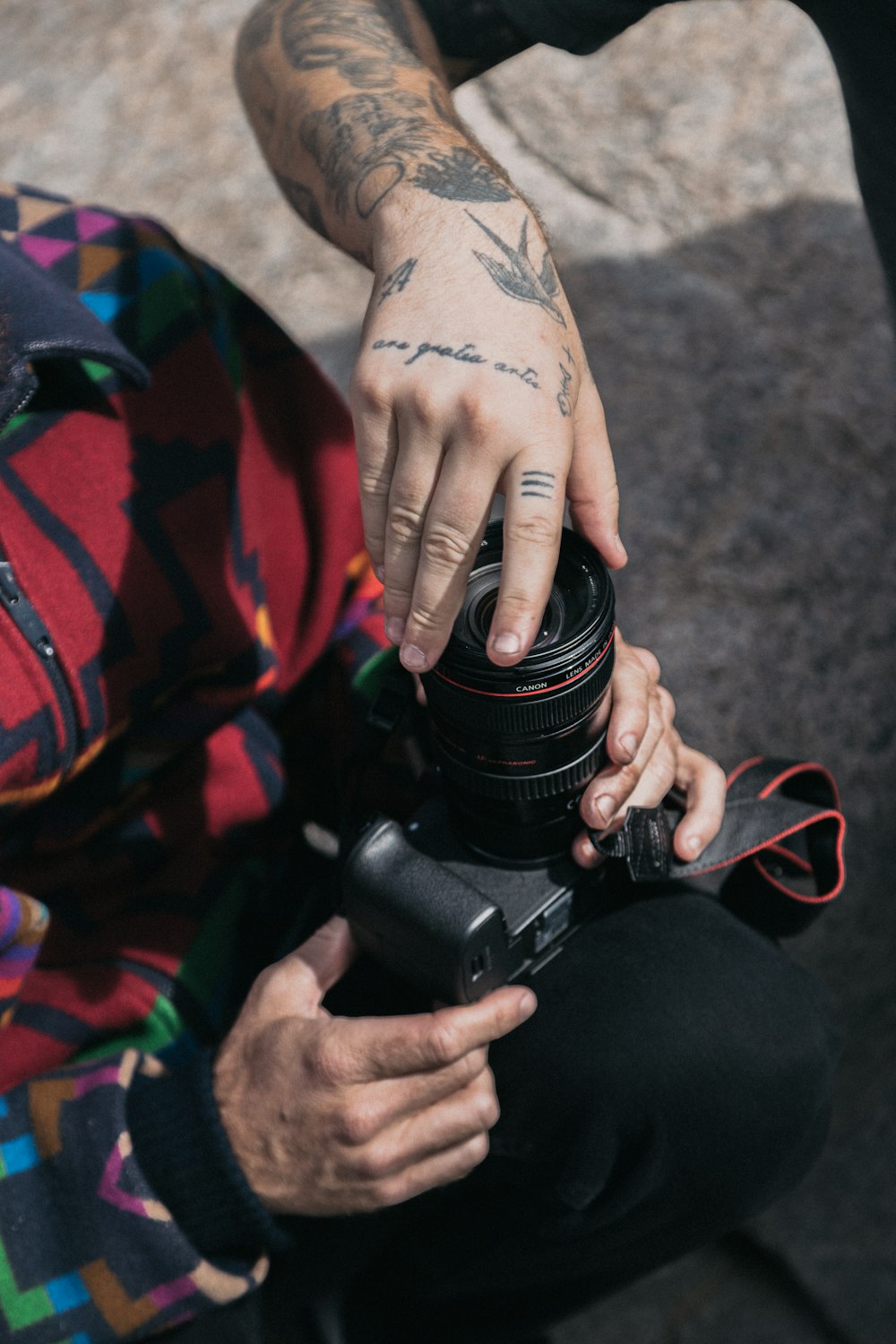 person in red and black long sleeve shirt holding black dslr camera