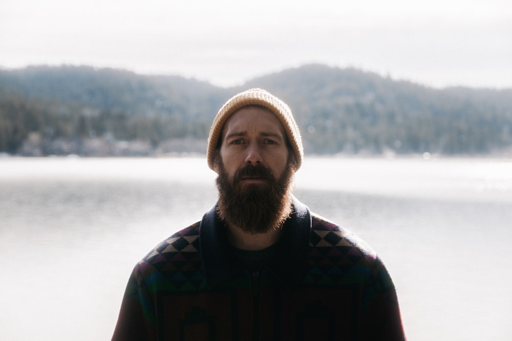 a man with a beard standing in front of a lake