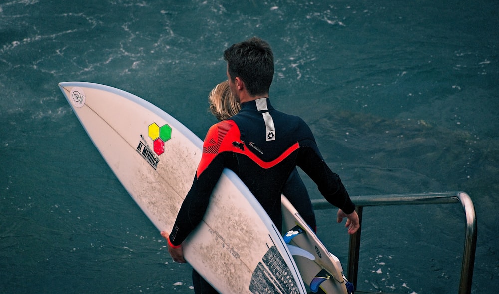 man in black and red vest holding white surfboard