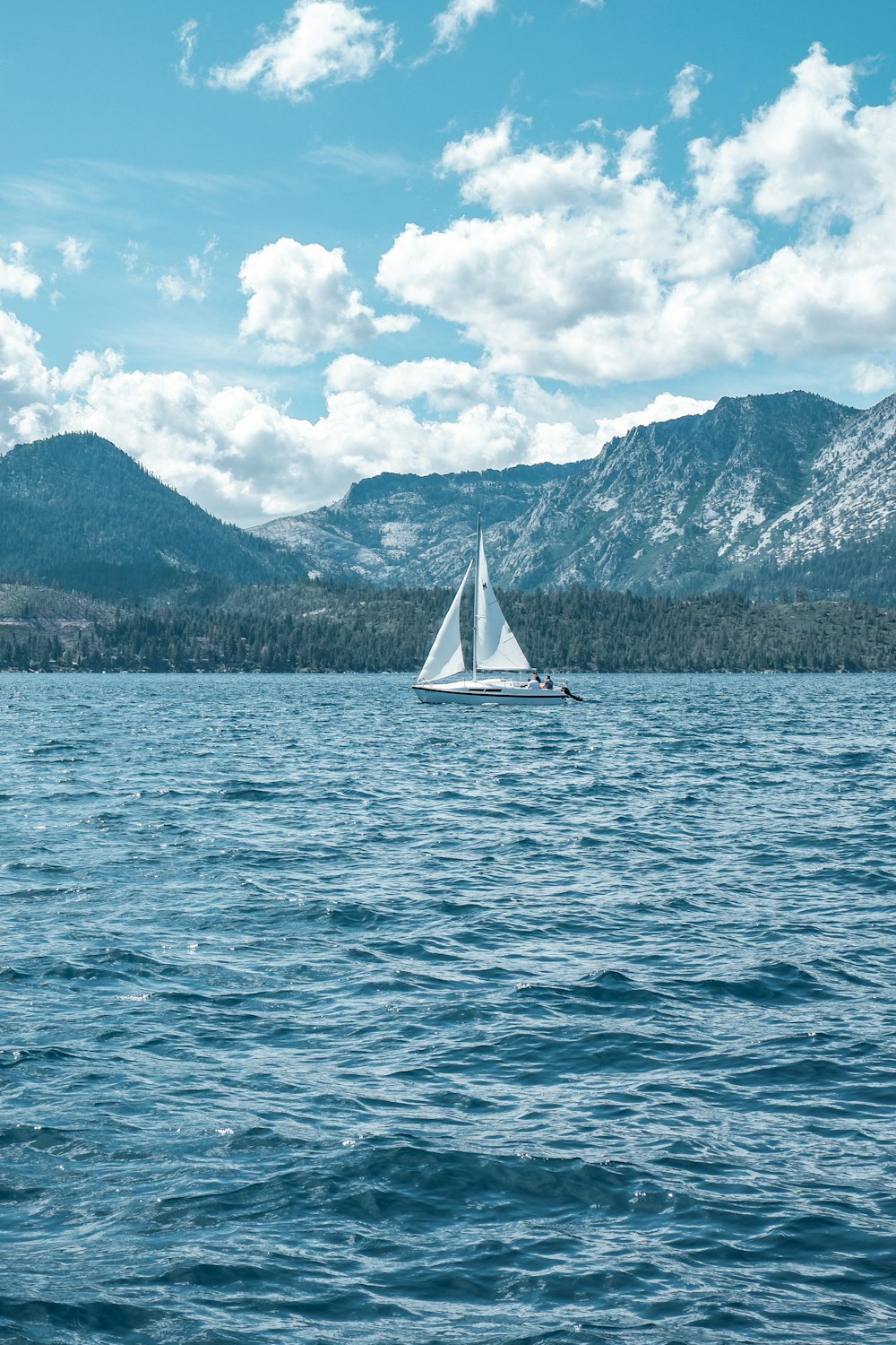 white sailboat on sea near mountain under white clouds and blue sky during daytime