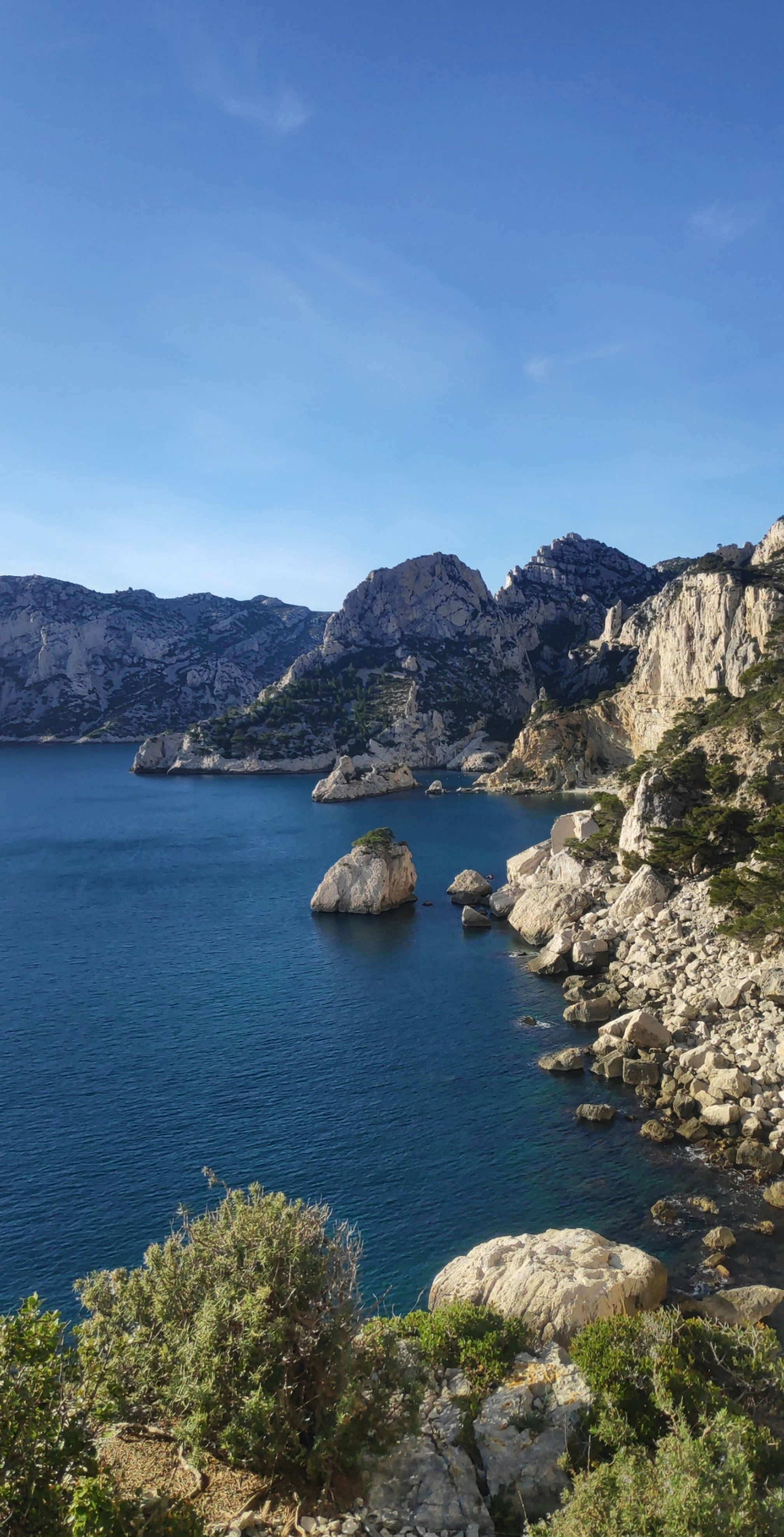 Brown rocky mountain beside blue sea under blue sky during daytime