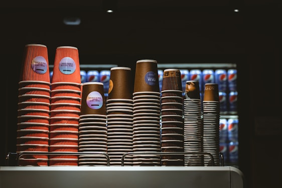 Stacked disposable cups and cutlery arranged on a wooden countertop in a bright kitchen setting.