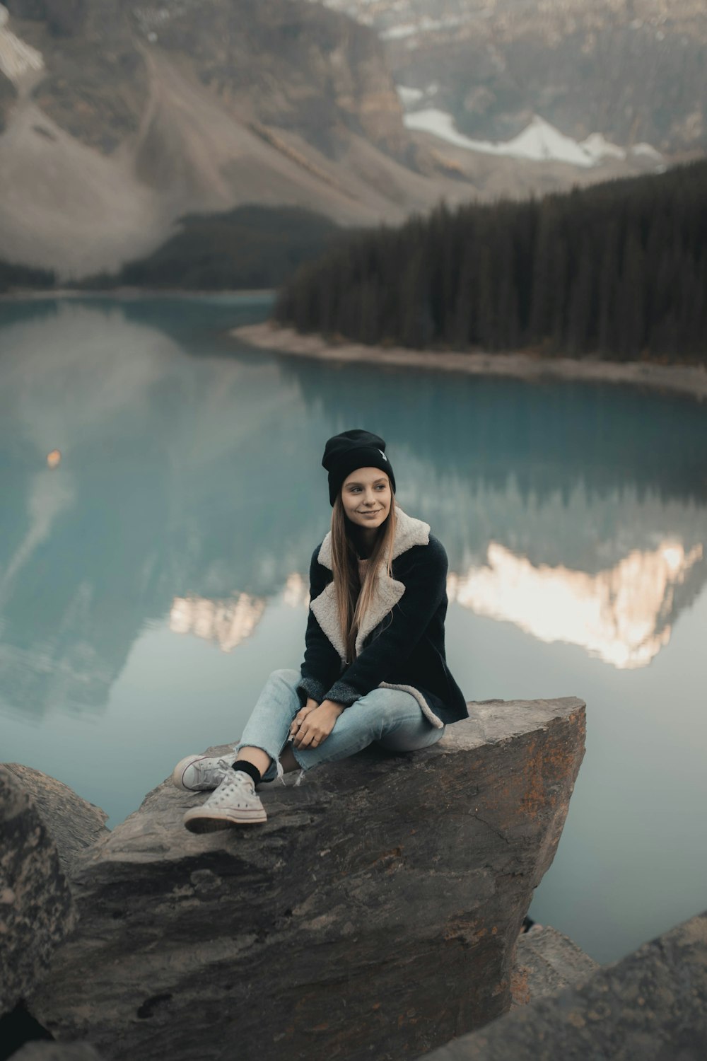 woman in black cardigan sitting on brown rock near body of water during daytime