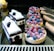 A variety of pastries, including berry-topped tarts with raspberries and blueberries, chocolate and cream cakes with cherries, and glazed éclairs, are displayed on a reflective black surface.