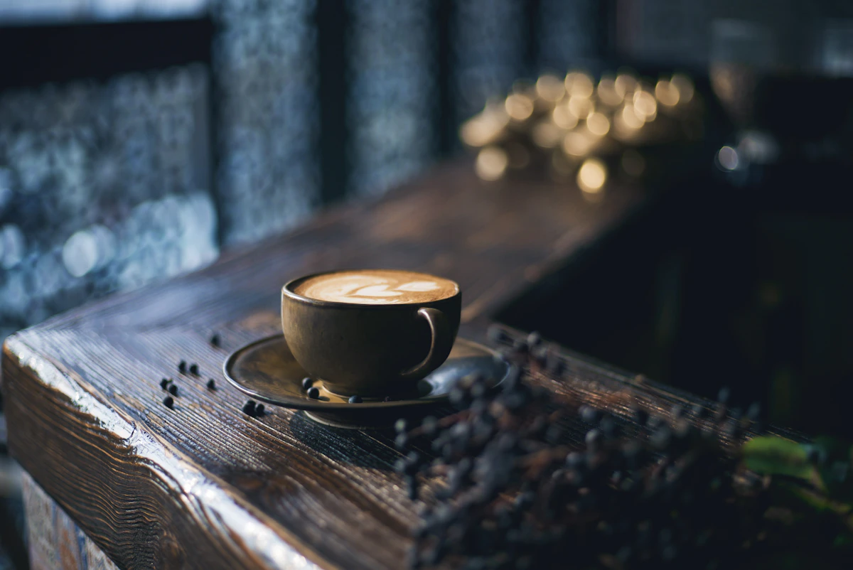 Coffee cup with latte art on wooden table with coffee beans scattered around