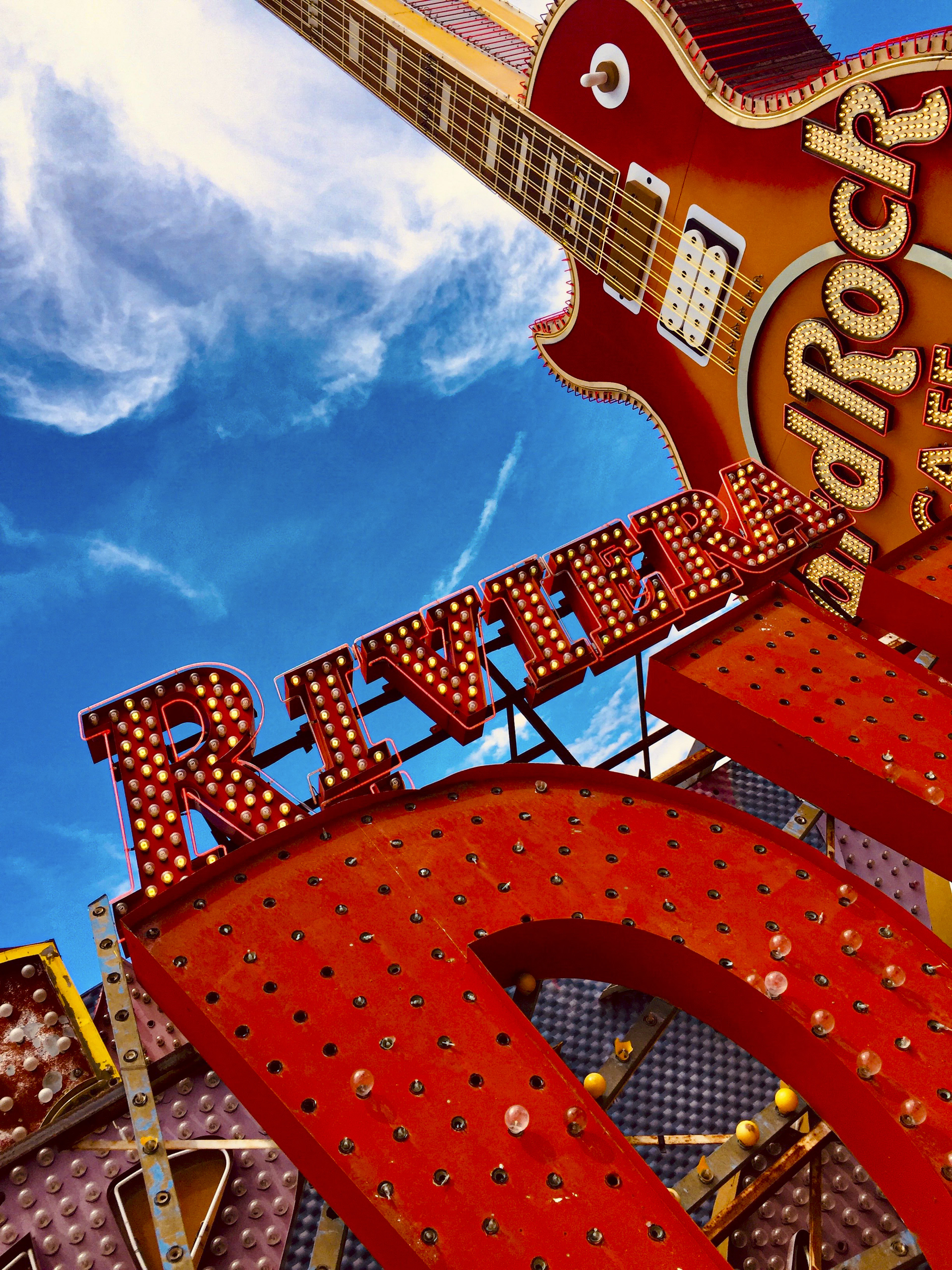 Vintage neon signs, including the Riviera marquee and a Hard Rock Cafe guitar, against a blue sky.