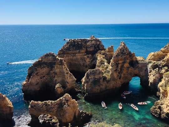 people swimming on sea near brown rock formation during daytime in Farol da Ponta da Piedade Portugal