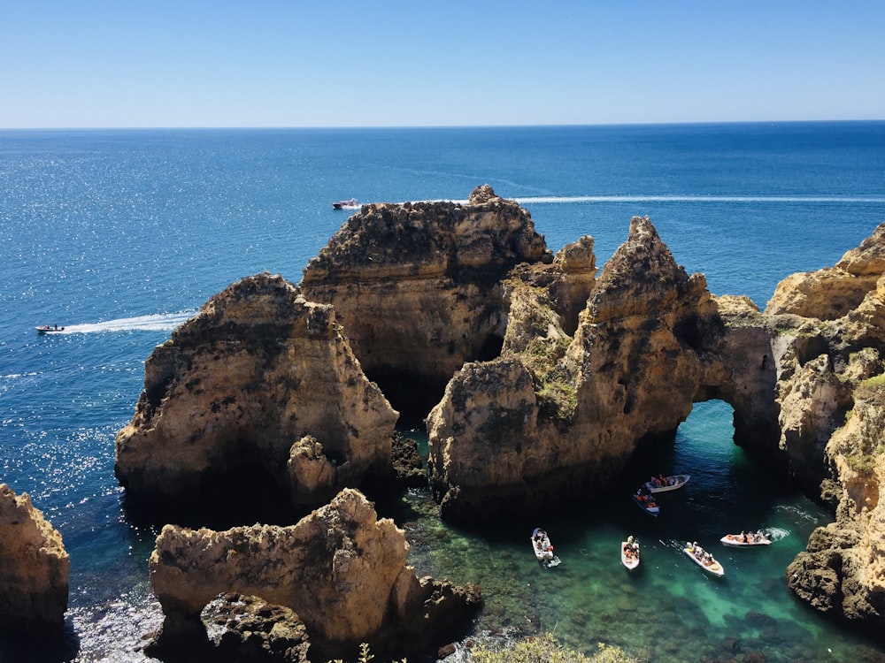 people swimming on sea near brown rock formation during daytime