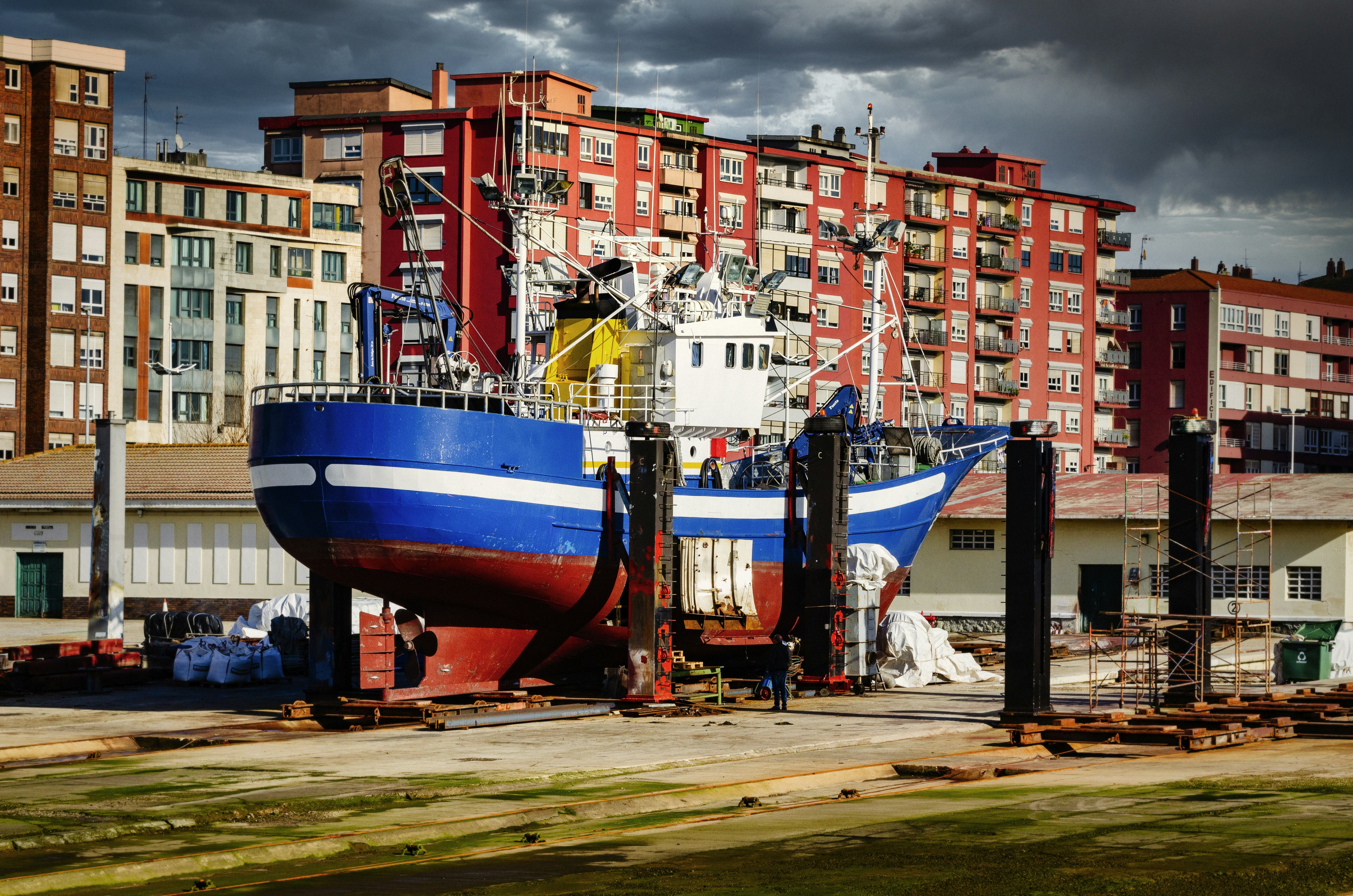 barco azul e branco vermelho na areia marrom perto de edifícios da cidade durante o dia