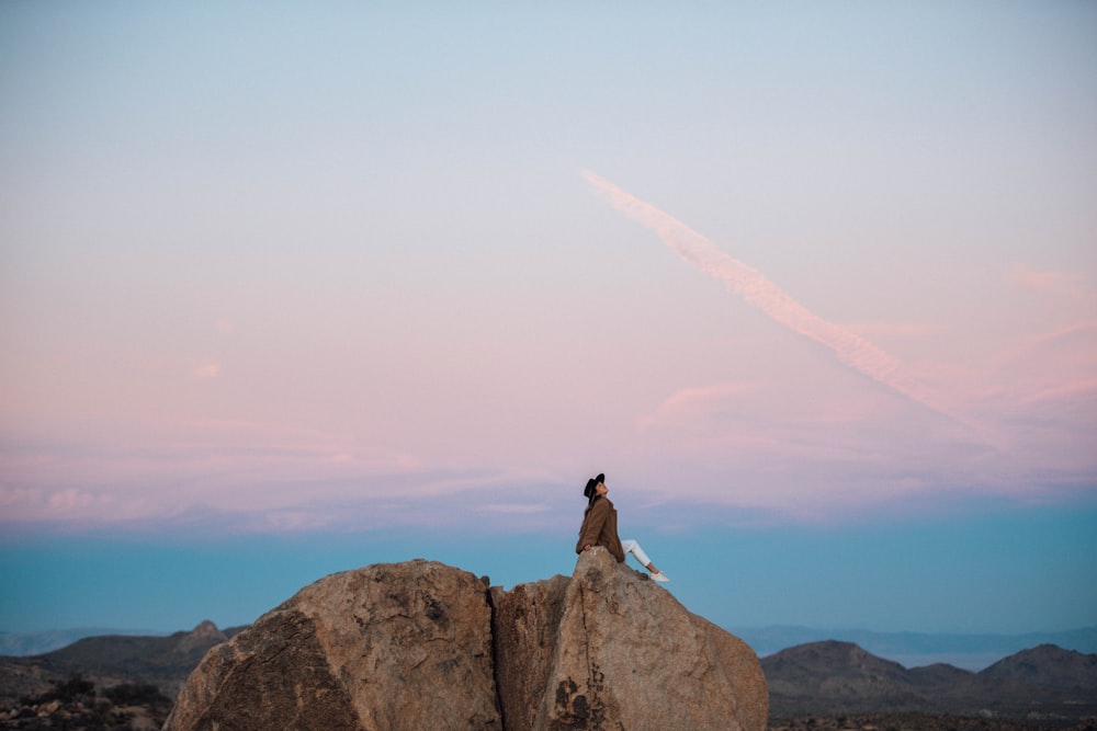 man in black jacket sitting on rock during daytime