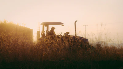 A farmer inspecting crops with a tractor in the background during golden hour.