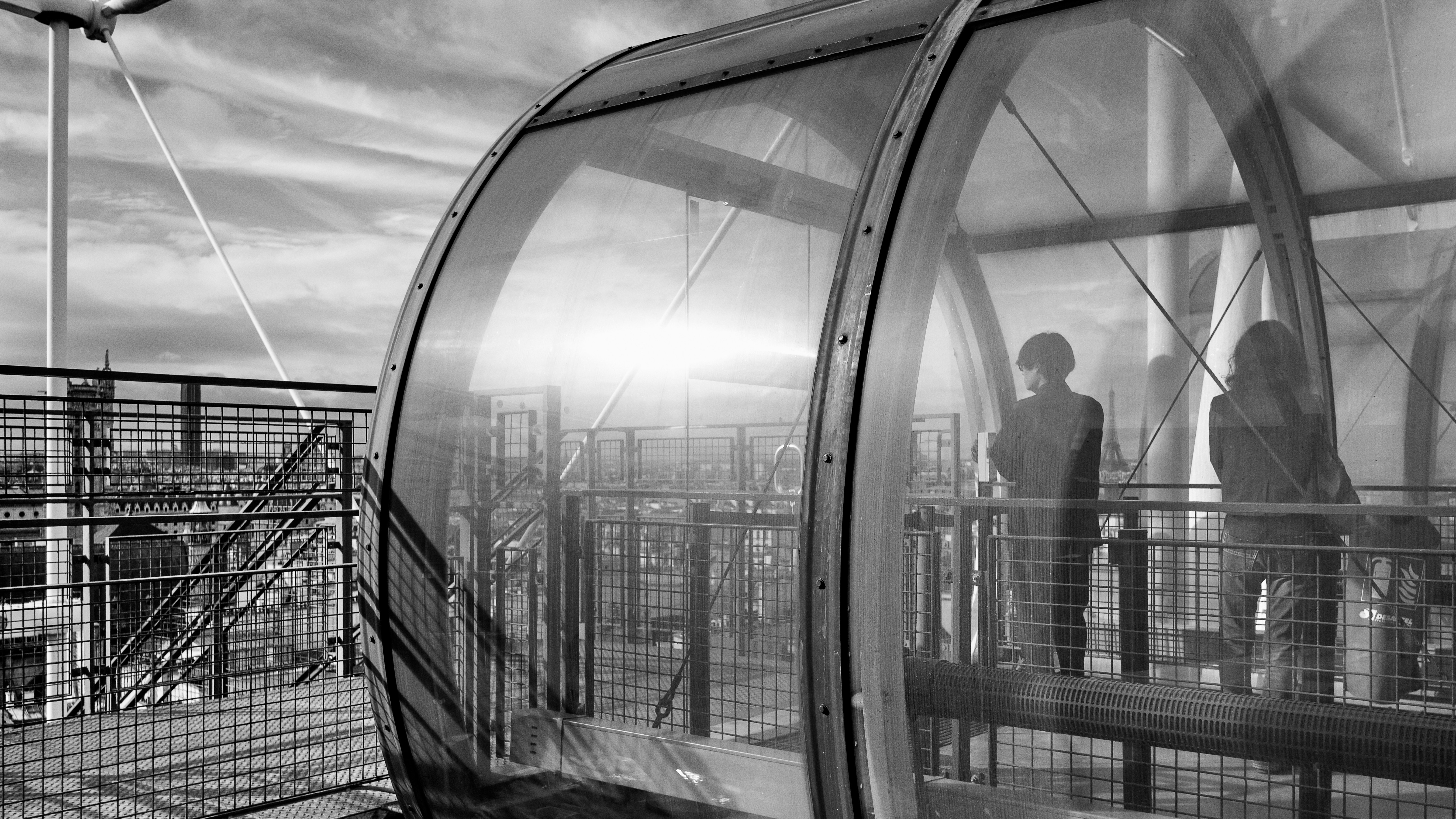 grayscale photo of man standing near glass window