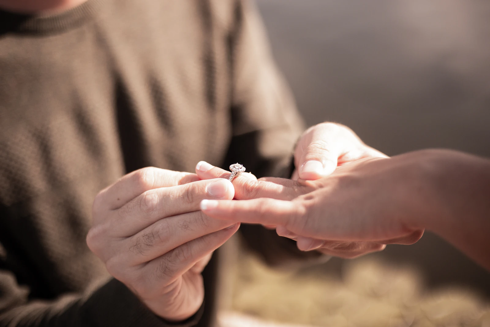 A man slips an engagement ring onto his partner's finger, outdoors
