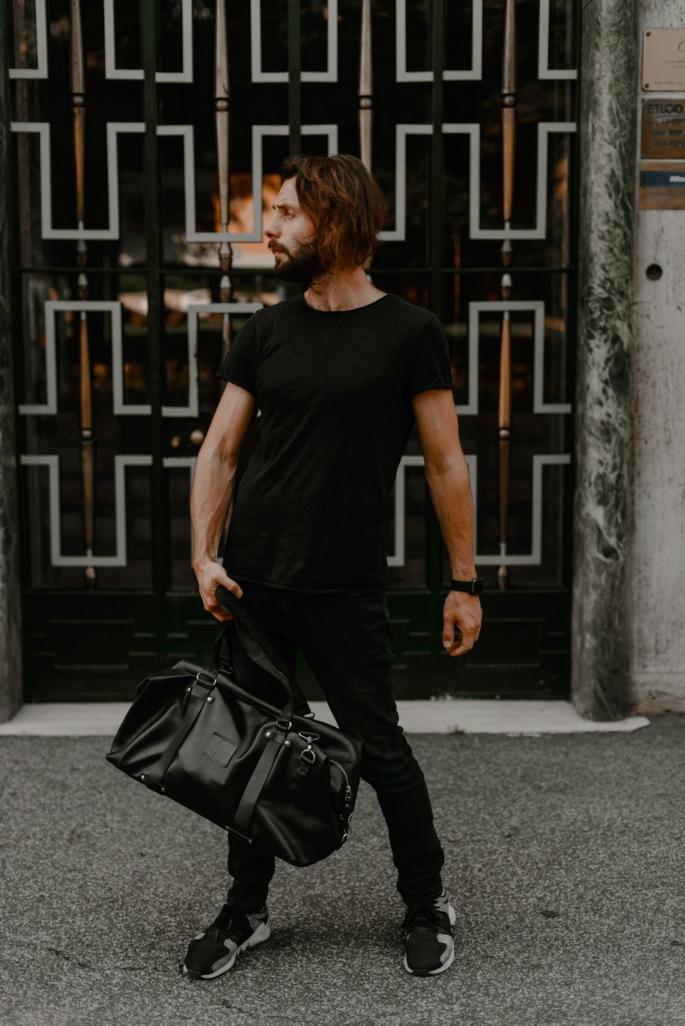 man in black crew neck t-shirt and black pants carrying black leather shoulder bag