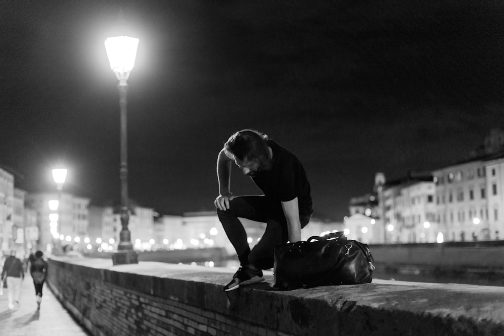 man in black t-shirt and black pants sitting on concrete wall