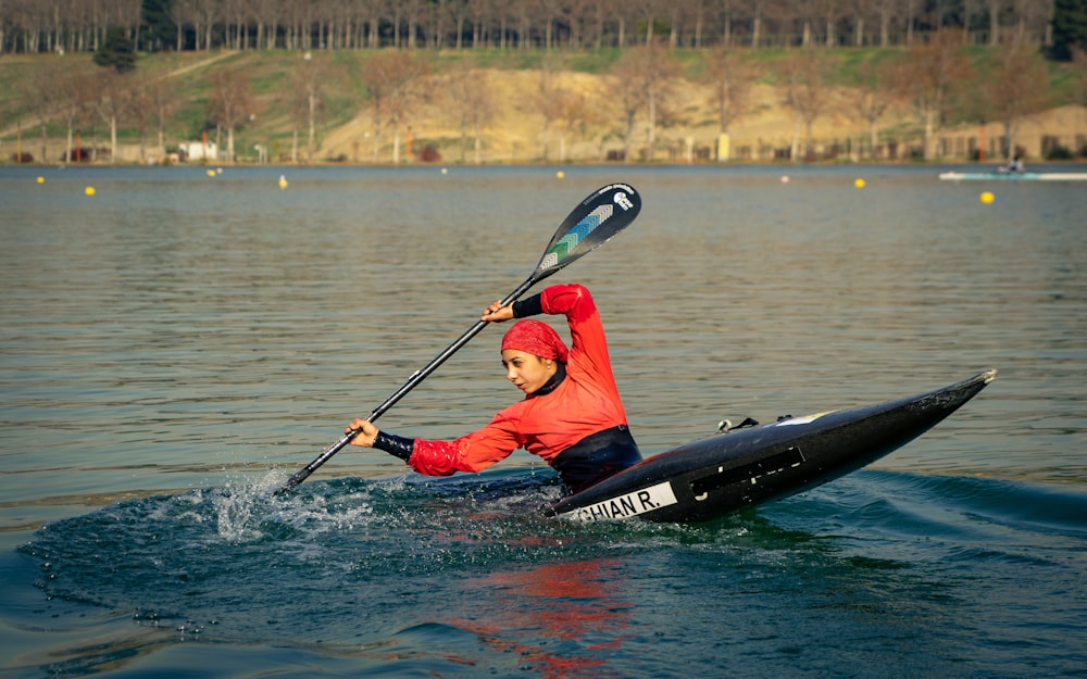 Hombre en chaqueta roja y negra montando en kayak negro en el cuerpo de agua durante el día