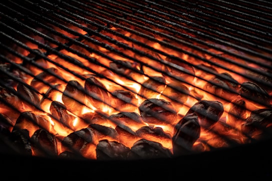 Glowing coals with bright orange flames are visible beneath a stainless steel grill, suggesting a setup prepared for barbecue or grilling.