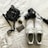 A neatly arranged collection of personal items on a white surface, including a black camera with a strap, white athletic shoes with visible brand text, a small black bag with a noticeable brand logo, a car key fob, and a decorated credit card.