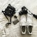 A neatly arranged collection of personal items on a white surface, including a black camera with a strap, white athletic shoes with visible brand text, a small black bag with a noticeable brand logo, a car key fob, and a decorated credit card.