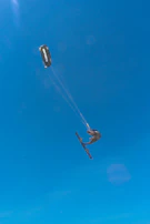 An advanced kite surfer performing a jump trick against a backdrop of palm trees and clear blue skies.