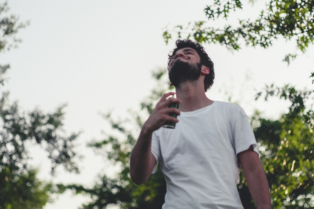 man in white crew neck t-shirt standing under tree during daytime