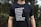 A person is wearing a black t-shirt with white text listing various regions and countries including Guatemala, Ecuador, Australia, England, Mexico, Zambia, Middle East, and North Africa. The background consists of greenery which seems to indicate an outdoor setting.