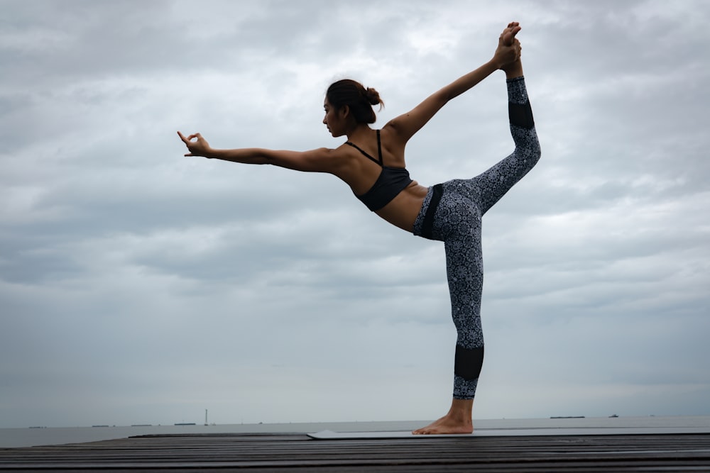 Femme en soutien-gorge de sport noir et leggings bleus faisant du yoga pendant la journée