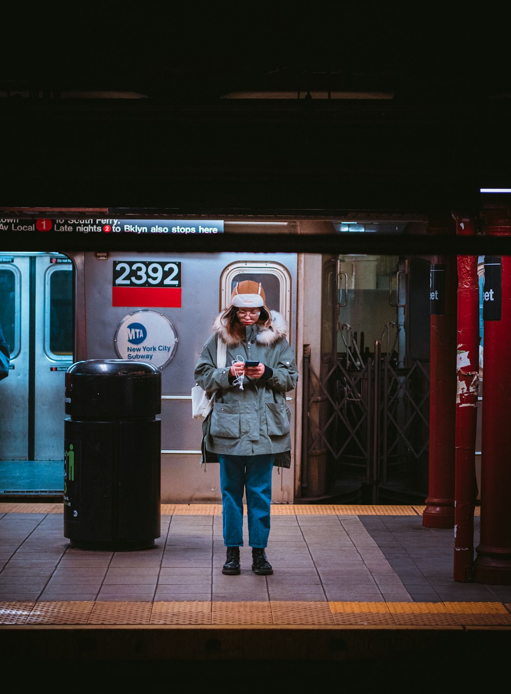 woman in gray jacket standing beside black trash bin