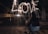 Two people are sitting closely together on a cobbled pathway at night, looking ahead at the word 'LOVE' spelled out in the air with sparklers. The atmosphere is intimate and illuminated by street lamps in the background.