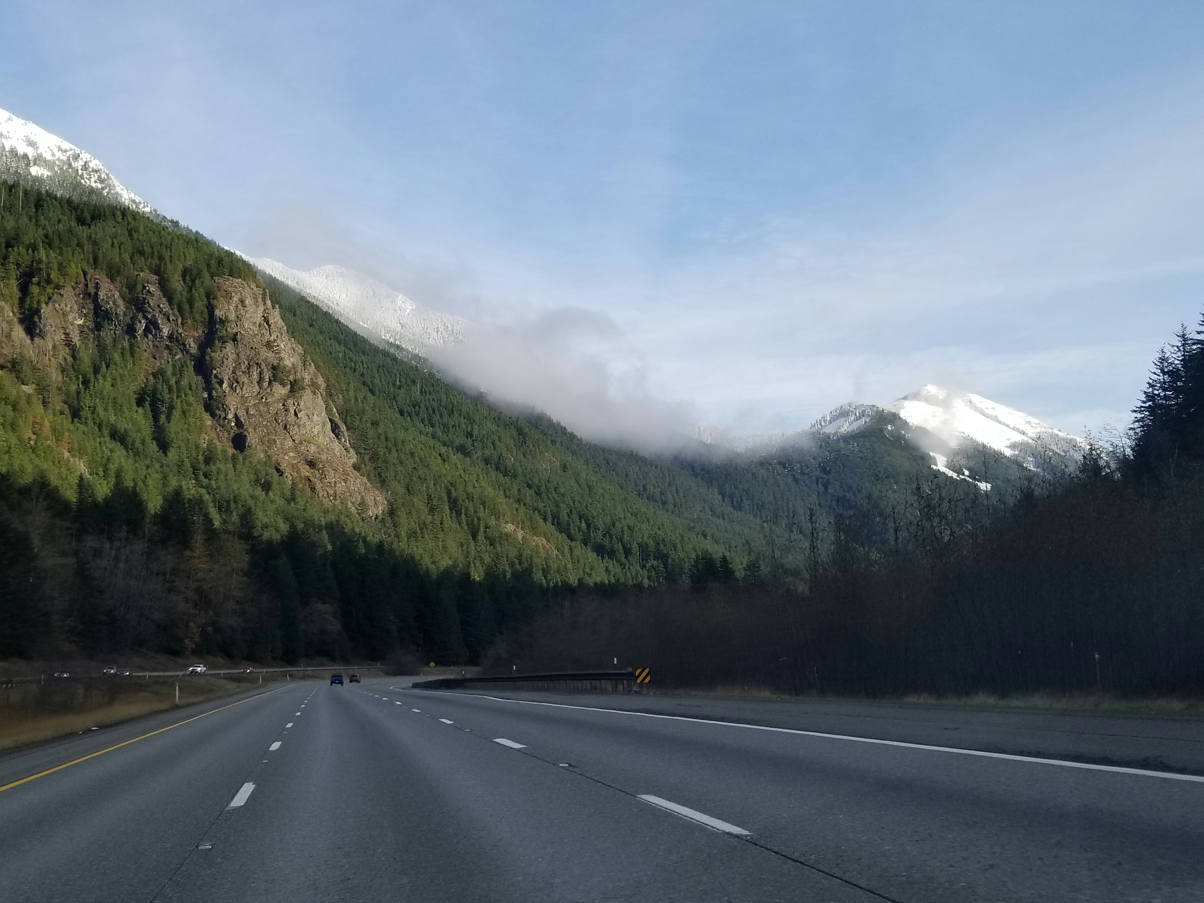 gray asphalt road between green trees and mountains during daytime