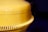 A close-up view of a large yellow industrial machine part with a smooth, rounded surface and a set of evenly spaced, vertical ridges at the bottom. The background is dark, emphasizing the bright yellow color.