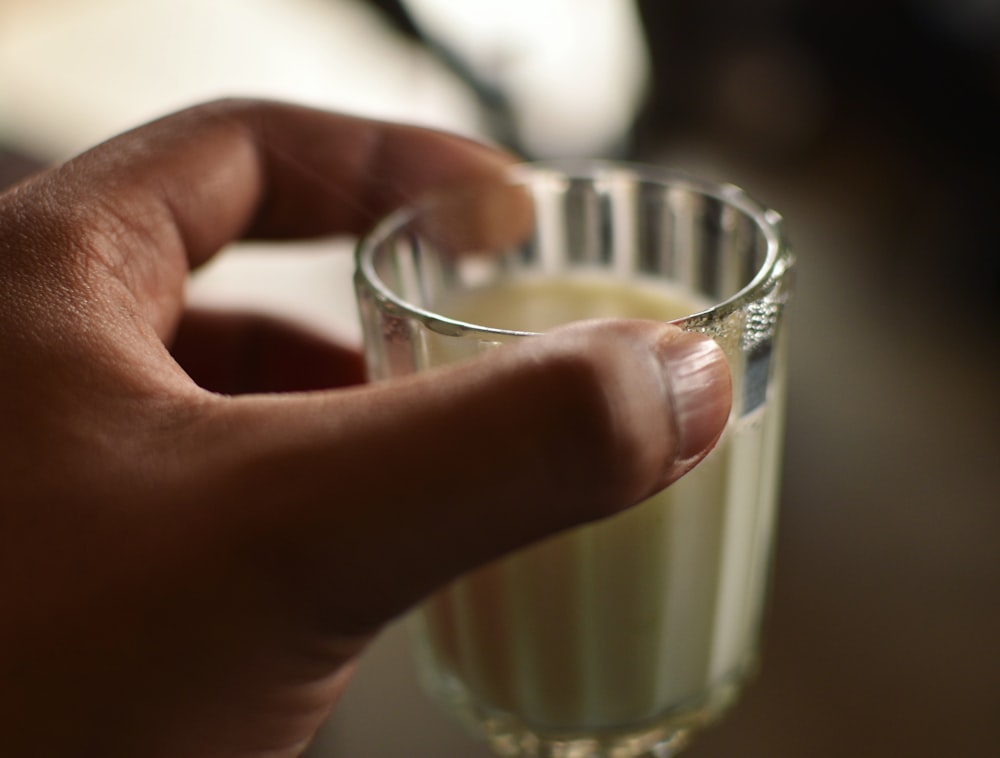 person holding clear drinking glass with white liquid