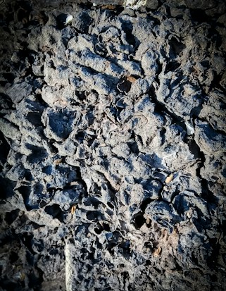 Rough, intricate textures of dark volcanic rock, appearing porous and rugged, with variations in shadow creating depth.