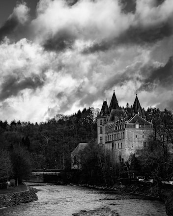 A dramatic black and white photo of a misty castle perched on a rugged cliff at dawn.