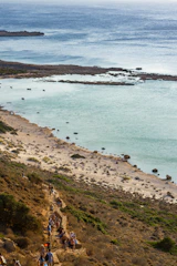 Coastal cliffs and turquoise waters with a small group walking along the shore.