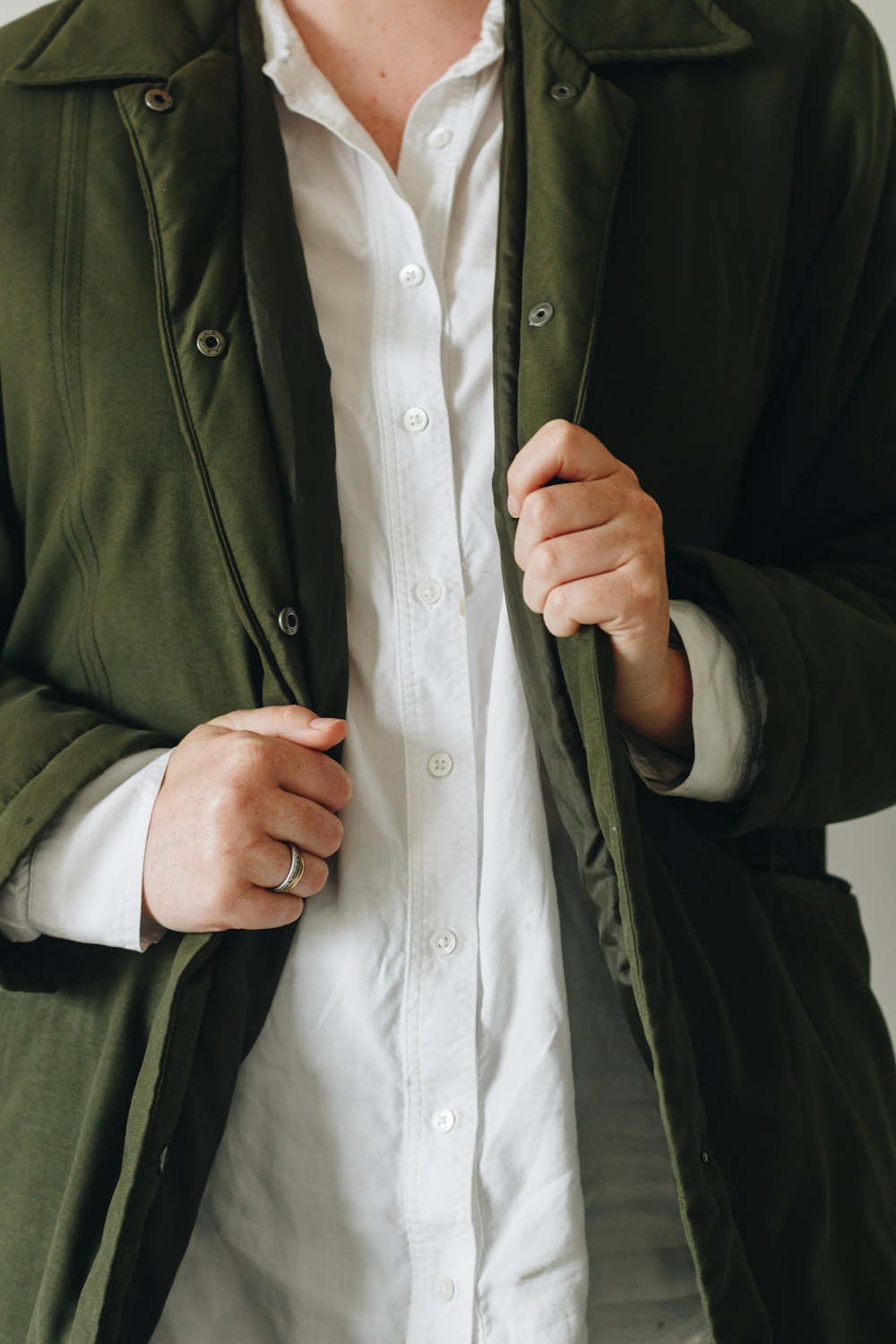 person in green coat holding white button up shirt