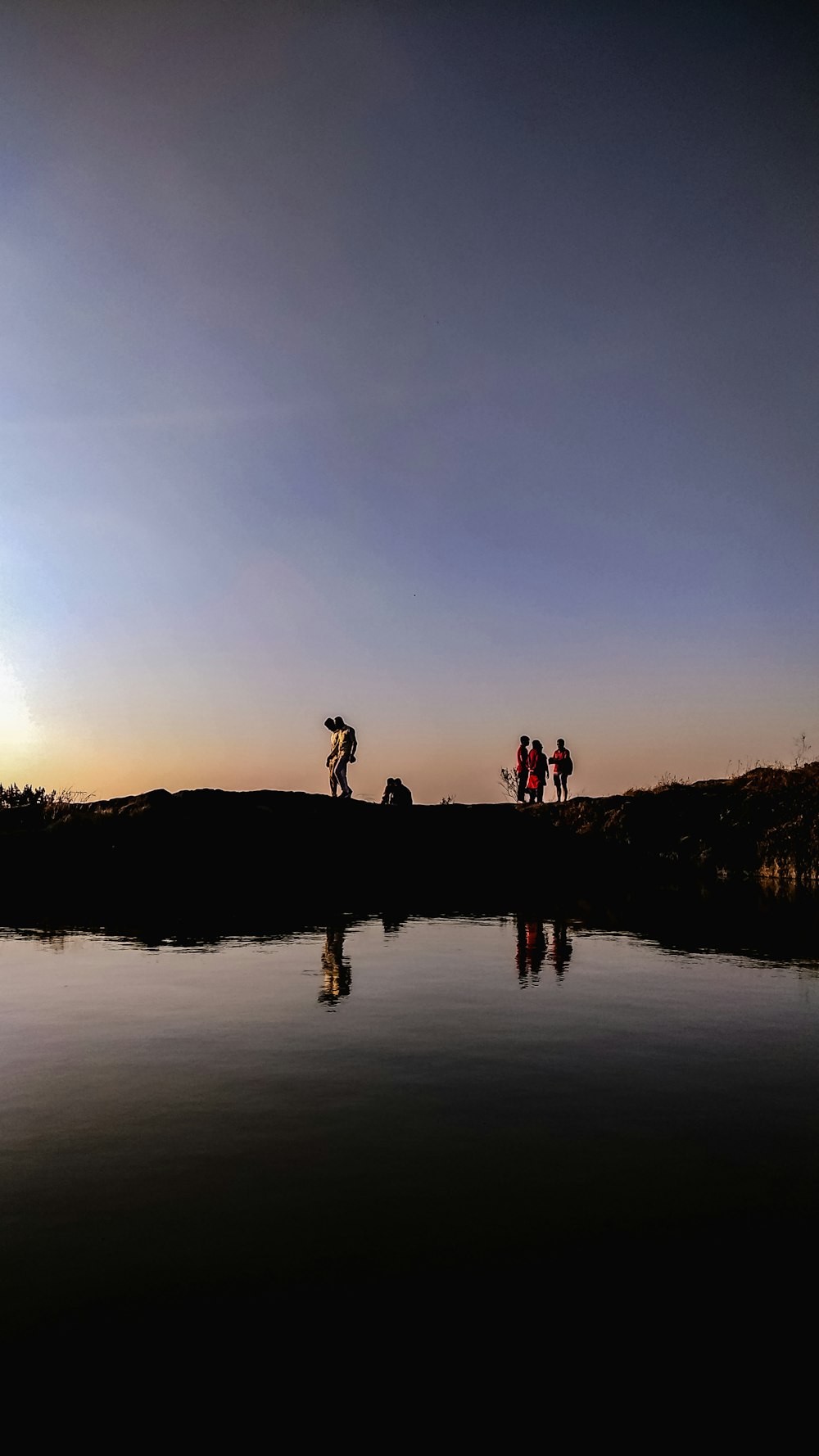 silhouette of people standing on water during sunset