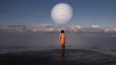 woman in brown coat standing on beach during daytime surreal teams background