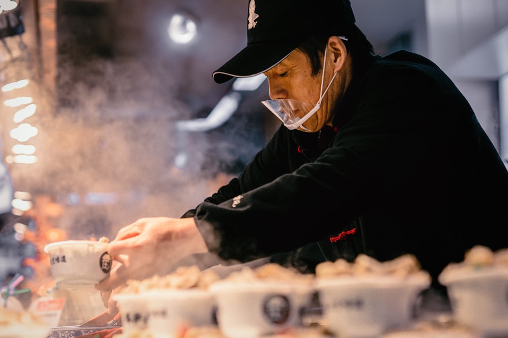 man in black jacket and black cap holding white plastic tray