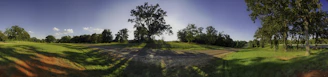 Wide view of a rural road crossing farmland with trees lining the path.