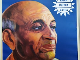 A colorful portrait of an elderly man with a serene expression, featuring a bald head and strong facial features set against a blue background. The logo 'Amar Chitra Katha' is visible in the top right corner.