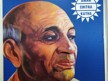 A colorful portrait of an elderly man with a serene expression, featuring a bald head and strong facial features set against a blue background. The logo 'Amar Chitra Katha' is visible in the top right corner.
