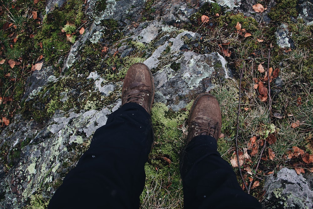 person in black pants and brown shoes standing on rocky ground