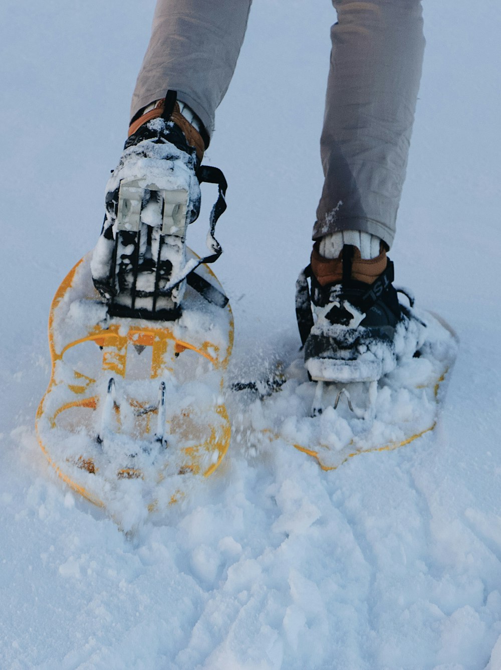 person in gray pants and black and orange hiking shoes standing on snow covered ground during