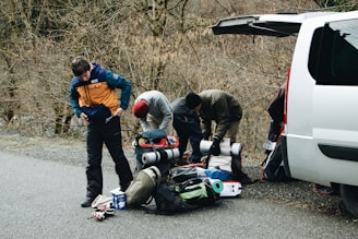 A happy family loading gear into a camper van under a bright blue sky.