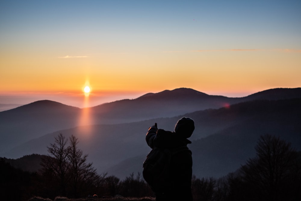 silhouette of person standing on mountain during sunset